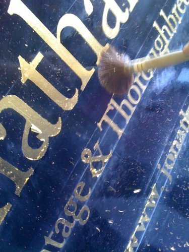 Gold leaf applied to signwritten lettering is dusted off to bright finish